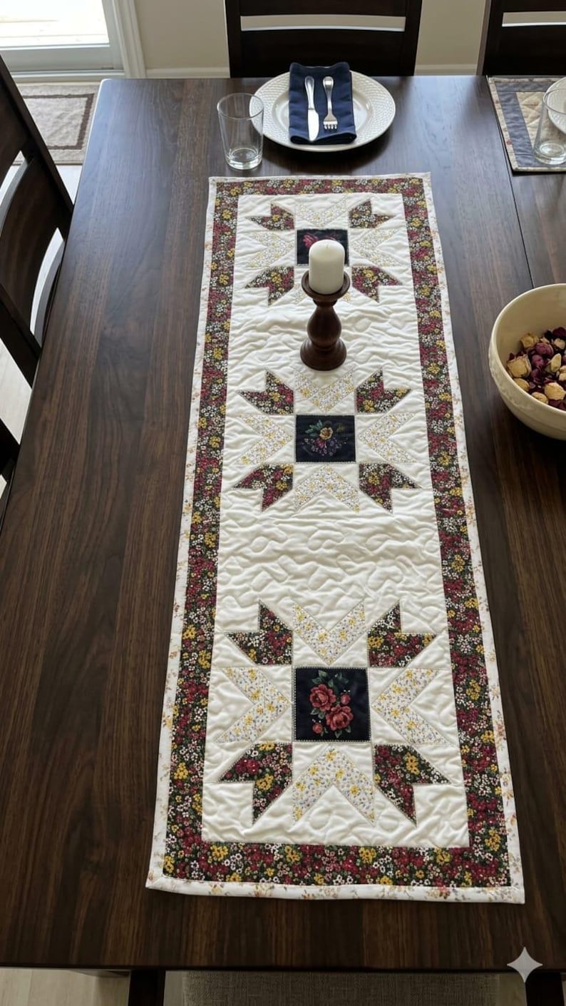 Puede incluir: Camino de mesa acolchado con un centro blanco y dise&ntilde;os de estrellas florales. Las estrellas est&aacute;n hechas de una mezcla de tela floral amarilla, roja y verde. Un borde floral oscuro enmarca el camino de mesa, de unos 30 cm de ancho.