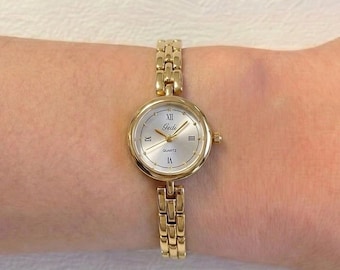 Relógio de pulso feminino de quartzo com caixa redonda dourada e prateada e pulseira ornamentada com contas.