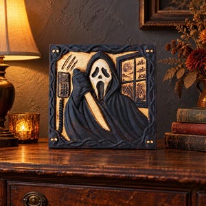 May include: A square wooden wall plaque featuring a carved relief of a hooded figure with a white ghost mask holding a knife. The scene includes a wall-mounted telephone and a window view. The frame is decorated with small skull motifs at corners.