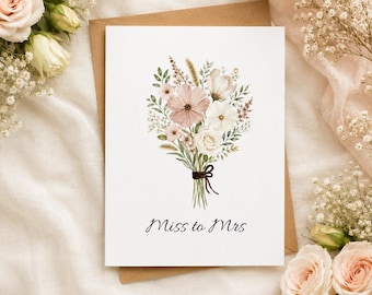 May include: A white greeting card featuring a watercolor illustration of a floral bouquet with pink and white flowers, green foliage, and a dark brown ribbon tie. The text "Miss to Mrs" is printed in black script below the floral arrangement.