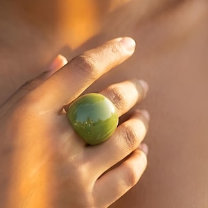Puede incluir: Un anillo grande, verde oliva con un acabado liso y brillante. La forma redondeada y el color vibrante del anillo son el punto focal, creando una pieza audaz. Un accesorio único.