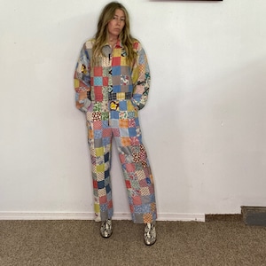 Può includere: Una tuta da lavoro in patchwork con una varietà di colori e motivi, tra cui rosso, blu, giallo e verde. La tuta ha una cerniera e maniche lunghe.