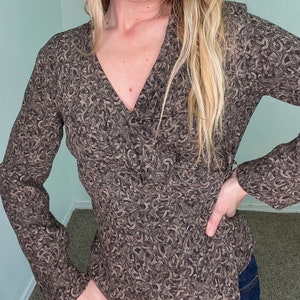 Könnte beinhalten: Eine langärmelige Wickelbluse in Braun und Schwarz mit V-Ausschnitt.