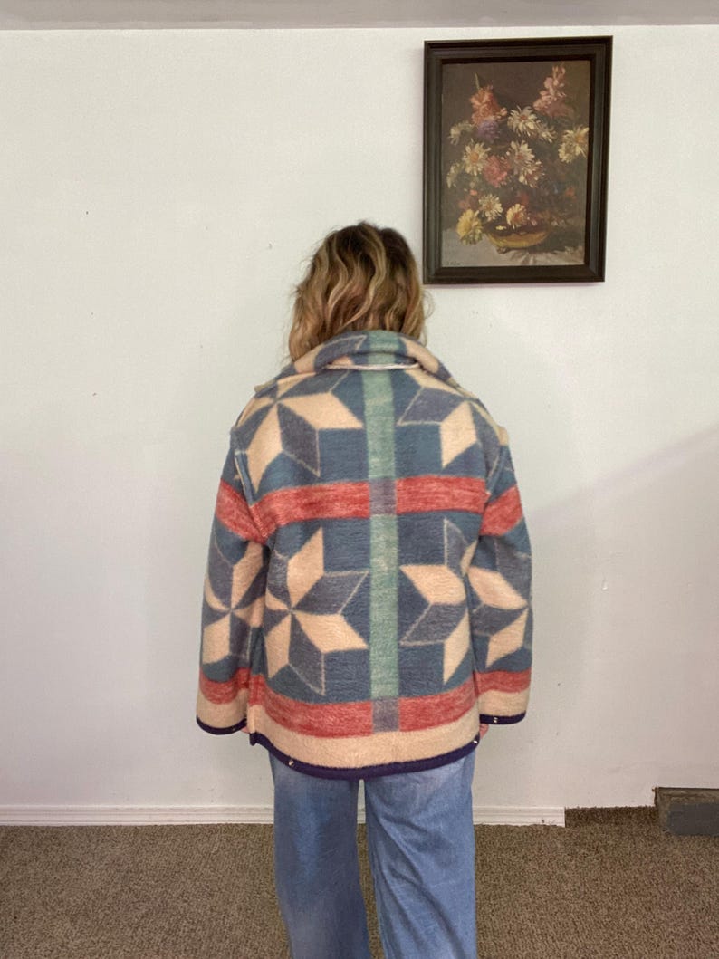 May include: A vintage-style jacket with a geometric star pattern in shades of blue, red, and beige. The jacket has a collared neckline and a button-up front. The jacket is worn with blue jeans.