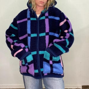 May include: A blue, purple, and teal plaid fleece jacket with a hood. The jacket has a zipper closure and pockets.