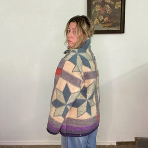 May include: A quilted jacket with a geometric star pattern in shades of blue, purple, and beige. The jacket has a high collar and a purple hem. The jacket is worn with blue jeans.