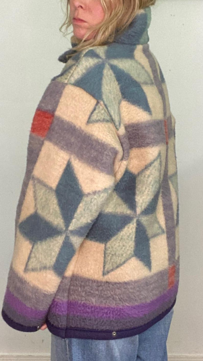 May include: A multi-colored jacket with a geometric star pattern. The jacket features a mix of colors including beige, blue, purple, and red. The jacket has a high collar and a button closure. The jacket is made of a soft, textured material.
