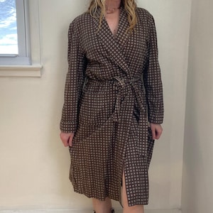 May include: A brown patterned robe with a wrap-around design and a matching belt. The robe features a repeating pattern of small white circles and has long sleeves. The knee-length robe is made of a lightweight fabric.