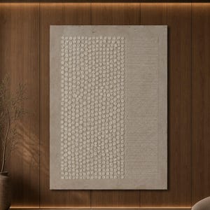 Puede incluir: Una gran pieza de arte mural rectangular con una superficie beige texturizada que presenta un patrón vertical de puntos circulares en relieve a la izquierda y una serie de líneas horizontales a la derecha, sobre una pared de madera oscura.