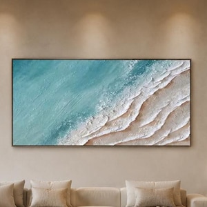 May include: A modern living room with a large, abstract painting of a beach scene in shades of blue, white, and beige. A beige sectional sofa, a dark wood coffee table, and a light beige rug complete the space. A vase of white flowers sits on the table.