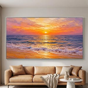 Op de afbeelding: Groot ingelijst olieverfschilderij van een zonsondergang boven de oceaan. Het kunstwerk toont een levendige oranje en gele lucht, met de zon die weerspiegelt in het water. Golven breken op een zandstrand, wat een serene kustscène creëert.