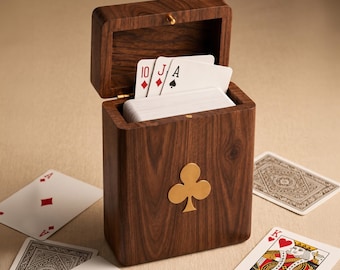 Könnte beinhalten: Eine dunkelbraune Spielkartenbox aus Holz mit Klappdeckel und einem goldfarbenen Metall-Kleeblatt-Emblem auf der Vorderseite. Die Box ist mit einem Kartenspiel gefüllt, wobei die Zehn Karo, der Bube Karo und das Pik-Ass zu sehen sind.