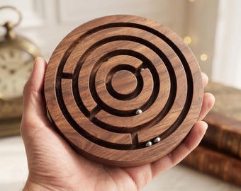 Könnte beinhalten: Ein kreisförmiges Holzlabyrinth-Puzzle mit einer dunkelbraunen Holzmaserung, das konzentrische kreisförmige Pfade und drei kleine silberne Metallkugeln aufweist, die in den geschnitzten Kanälen des Spielbretts liegen.