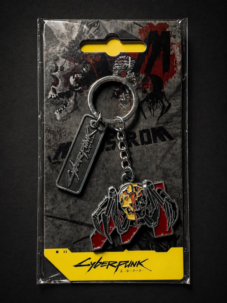 May include: Cyberpunk 2077 keychain featuring a stylized spider-like creature with red and yellow accents. The keychain includes a metal tag with the game's logo. The packaging is a clear plastic with a yellow label and the game's title.