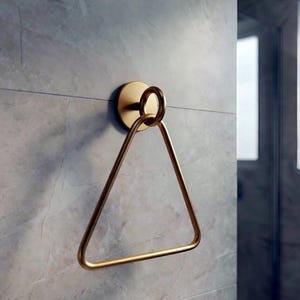 Op de afbeelding: Een goudkleurige handdoekring met een driehoekig ontwerp. De ring is gemonteerd op een cirkelvormige basis en aan de muur bevestigd. De badkamerarmatuur is gemaakt van metaal en heeft een moderne uitstraling.
