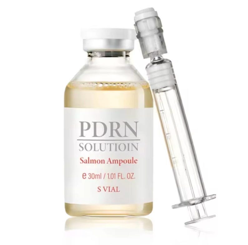 May include: A clear glass bottle with a white cap and label, containing a yellow liquid. The label reads "PDRN SOLUTION Salmon Ampoule e 30ml / 1.01 FL. OZ. S VIAL." A clear syringe is positioned next to the bottle.