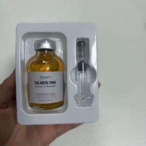 May include: A skincare product set featuring a small amber glass bottle with a silver cap and a clear syringe. The bottle is labeled "Zyvarn Salmon DNA Serum Ampoule". The set is packaged in a white plastic tray.
