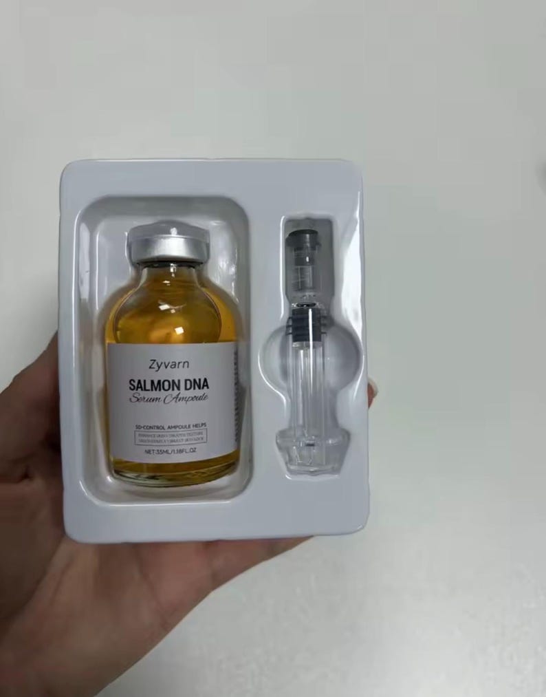 May include: A skincare product set featuring a small amber glass bottle with a silver cap and a clear syringe. The bottle is labeled "Zyvarn Salmon DNA Serum Ampoule". The set is packaged in a white plastic tray.