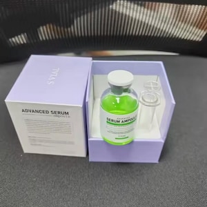 May include: A skincare product set featuring a green serum ampoule in a clear glass bottle with a white cap, displayed in a light purple box. The box is open, revealing the ampoule and a clear glass vial. The box is labeled "ADVANCED SERUM ampoule".
