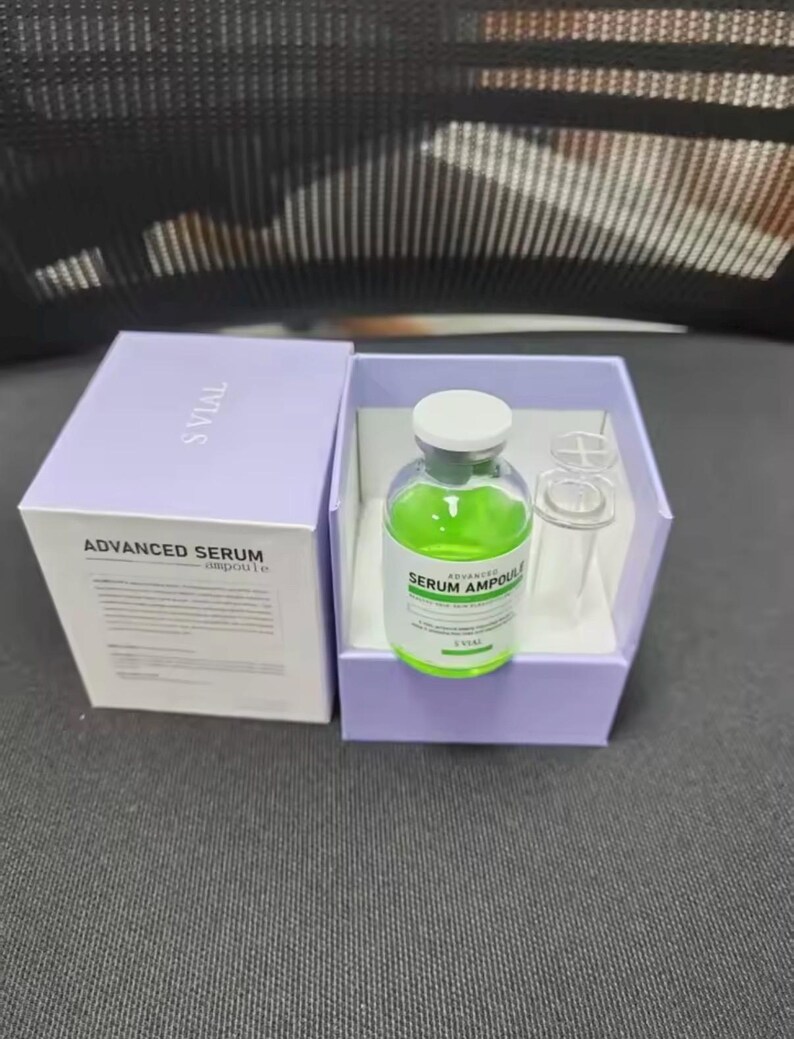 May include: A skincare product set featuring a green serum ampoule in a clear glass bottle with a white cap, displayed in a light purple box. The box is open, revealing the ampoule and a clear glass vial. The box is labeled "ADVANCED SERUM ampoule".