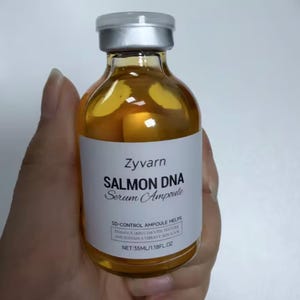 May include: A clear glass bottle of Zyvarn Salmon DNA Serum Ampoule, held in a hand. The bottle has a silver cap and a white label with black text. The label reads "SD-CONTROL AMPOULE HELPS ENHANCE SKIN'S SMOOTH TEXTURE AND SUSTAIN A VIBRANT SKIN GLOW". The bottle contains 35ml/1.18 fl oz.