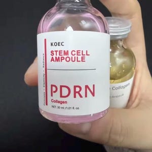 May include: A clear glass bottle with a pink liquid inside, labeled "KOEC STEM CELL AMPOULE PDRN Collagen." The bottle contains 30 ml / 1.01 fl. oz. of product. The bottle is held in a hand.