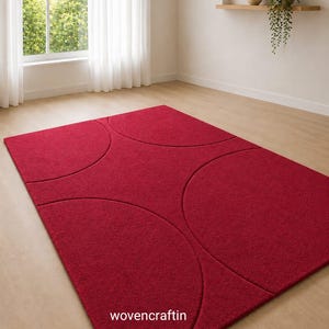 Könnte beinhalten: Ein rechteckiger Teppich in tiefem Rot mit einem geschnitzten geometrischen Muster aus sich überschneidenden Kreisbögen. Die Oberfläche hat einen strukturierten Flor und der Text "wovencraftin" ist in Weiß im unteren Bereich aufgedruckt.