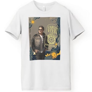 May include: White t-shirt featuring a graphic of Carlos Vives, with the text "CARLOS VIVES TOUR AL SOL - USA 2020". The design includes a portrait of Carlos Vives, sun and floral elements in a vintage style.
