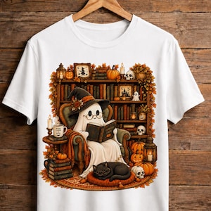 Könnte beinhalten: Ein weißes T-Shirt mit einer Grafik eines Geistes mit Hexenhut und Brille, der in einem Sessel sitzt und ein Buch mit dem Titel Ghostly Tales liest. Die Szene zeigt zudem eine schwarze Katze, Kürbisse, Totenköpfe, Kerzen und ein Bücherregal.