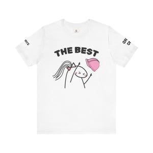 May include: White t-shirt with a cartoon illustration of a stick figure with long hair and a pink hat. The text "THE BEST" is above the figure. Text on the sleeves reads "WAYS" and "ON IO".