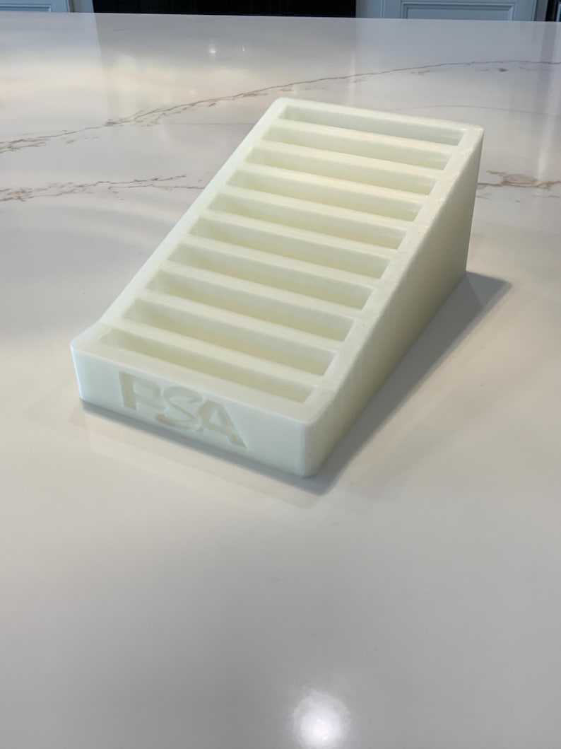 May include: A white, stepped display stand with the letters "PSA" embossed on the front. The stand has multiple horizontal slots, resembling a staircase. The object is made of a solid, opaque material.