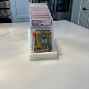 May include: A stack of graded sports trading cards in protective cases, displayed on a white holder. The top card features Patrick Mahomes, with the text "2017 Panini Donruss Optic" visible. The holder is white and has the "PSA" logo.