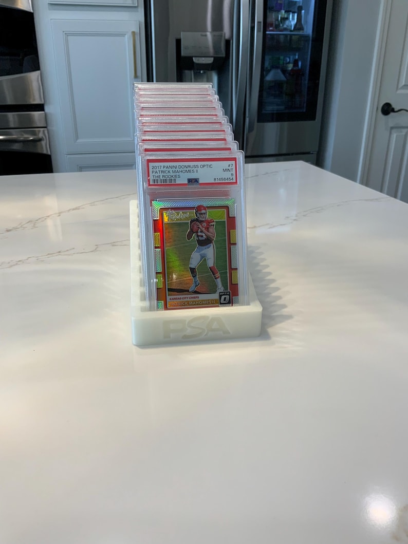 May include: A stack of graded sports trading cards in protective cases, displayed on a white holder. The top card features Patrick Mahomes, with the text "2017 Panini Donruss Optic" visible. The holder is white and has the "PSA" logo.
