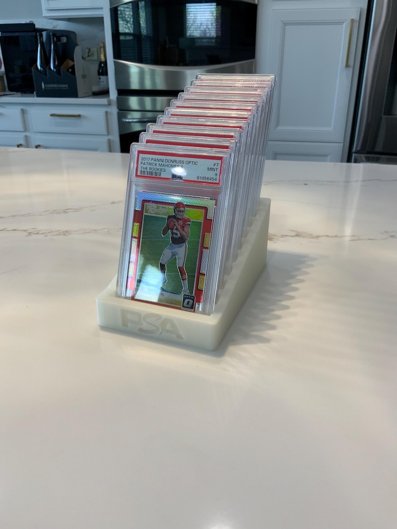 May include: A collection of graded sports cards in protective cases, displayed in a white holder. The cards feature a football player in a red uniform. The holder is labeled with the letters "PSA".