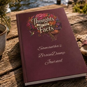 May include: A maroon hardcover journal featuring a floral brain illustration with the text "Thoughts Are Not Facts" and "Samantha's BrainDump Journal" printed on the front cover. The book has a smooth finish and white pages visible at the edge.