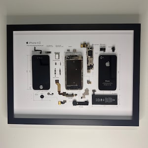 May include: A framed deconstructed iPhone 4S display featuring the black front screen, rear glass panel, logic board, battery, and various internal components arranged on a white background with technical labels and the text iPhone 4S.