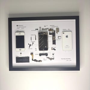 May include: A framed deconstructed white iPhone 4 display featuring the front screen, back casing, battery, and internal components arranged on a white background with labels, technical specifications, and the text "Stay hungry, Stay foolish."