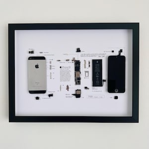 May include: A framed deconstructed iPhone SE display featuring the silver back casing, black front screen, battery, logic board, and various internal components arranged on a white background with technical labels and a quote by Steve Jobs.