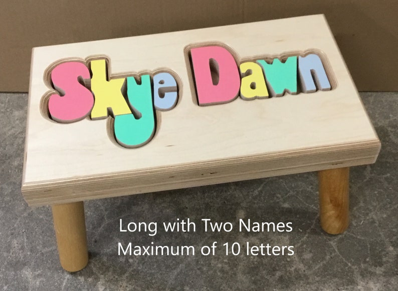Step stool with four legs that has the name Skye Dawn puzzled into the top where each letter is a puzzle piece.  Letters are painted in bright pastel colors in a rainbow pattern starting with pink.  2 name size holds 2 name up to 10 letters maximum.