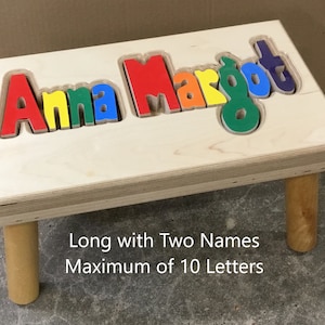 Step stool with four legs that has the name Anna Margot puzzled into the top where each letter is a puzzle piece.  Letters are painted in bright primary colors in a rainbow pattern starting with red.  2 names up to 10 letters maximum.