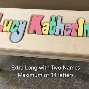 Step stool with 4 legs that has the name Lucy Katherine puzzled into the top where each letter is a puzzle piece.  Letters are painted in pastel colors in a rainbow pattern starting with pink.  2 name size holds 2 names with up to 14 letters maximum.