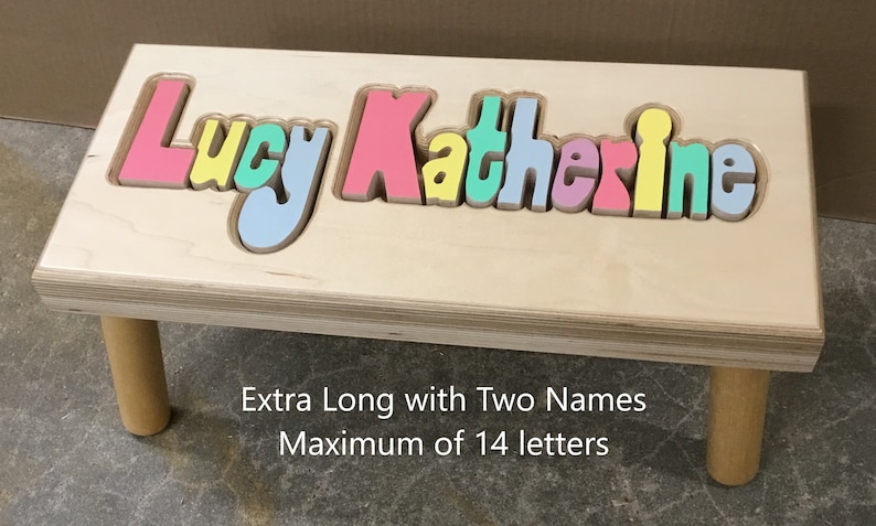 Step stool with 4 legs that has the name Lucy Katherine puzzled into the top where each letter is a puzzle piece.  Letters are painted in pastel colors in a rainbow pattern starting with pink.  2 name size holds 2 names with up to 14 letters maximum.