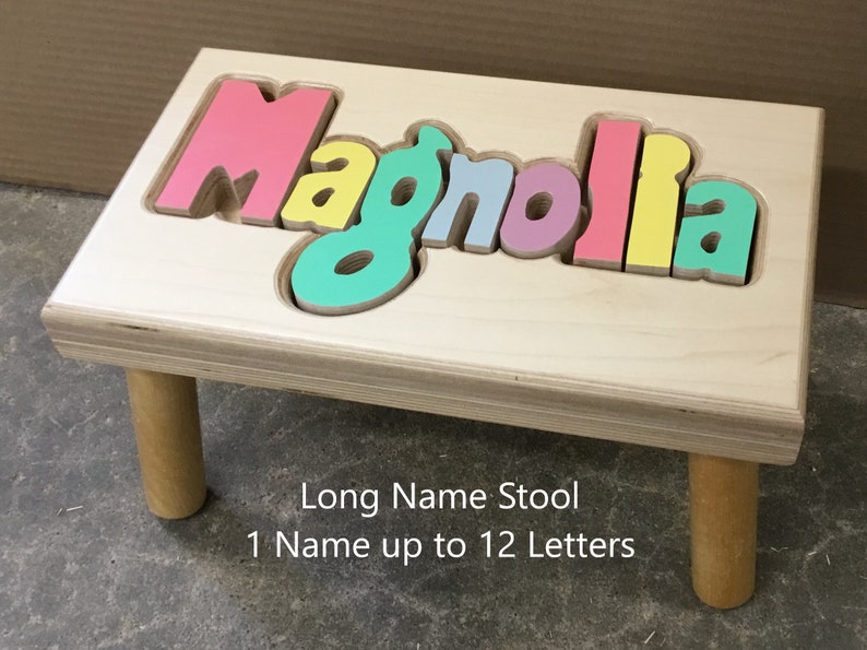 Step stool with four legs that has the name Magnolia puzzled into the top where each letter is a puzzle piece.  Letters are painted in bright pastel colors in a rainbow pattern starting with pink.  Long size holds 1 name up to 12 letters maximum.