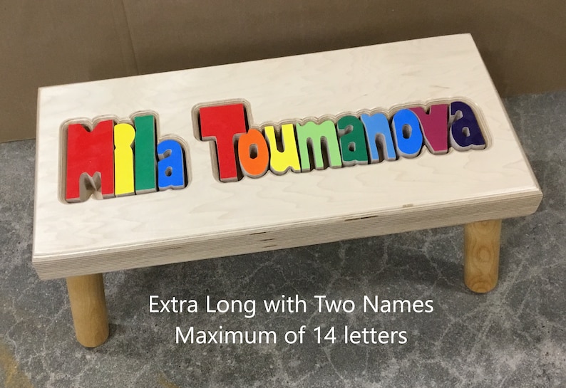 Step stool with 4 legs that has the name Mila Toumanova puzzled into the top where each letter is a puzzle piece.  Letters are painted in primary colors in a rainbow pattern starting with red.  2 name size holds 2 names with up to 14 letters maximum.
