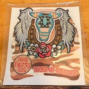 May include: Embroidered patch featuring a winged bull skull, horseshoe, and floral accents. The design incorporates turquoise, brown, and red colors. The text "Patch Party Girl" and "Trucker Hat Accessories" are also visible.