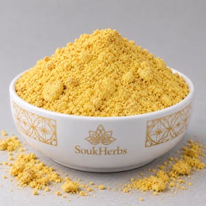 Könnte beinhalten: Eine weiße Keramikschale gefüllt mit einem Haufen feinem gelben Pulver. Die Schale ist mit einem goldenen geometrischen Muster und dem in Gold gedruckten Text SoukHerbs versehen. Kleine Klumpen des gelben Pulvers liegen um die Schale.
