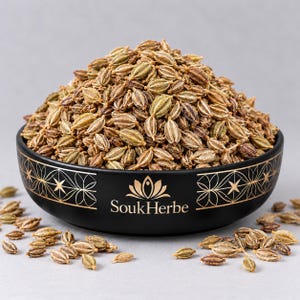 Puede incluir: Un cuenco de cerámica negra lleno de un montón de semillas de ajwain secas de color marrón claro. El cuenco presenta un patrón geométrico dorado y el texto SoukHerbe impreso en oro. Varias semillas sueltas rodean la base del cuenco.