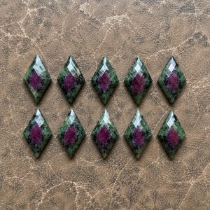 May include: Ten faceted diamond-shaped gemstones arranged in two rows of five. Each stone features a deep magenta center surrounded by a mottled green and black border, with a polished, multi-faceted surface reflecting light across the top.