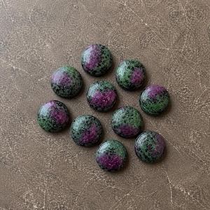 May include: Ten round, polished cabochons of ruby zoisite stone. Each piece features a smooth, domed surface with a distinct mottled pattern of vibrant magenta-pink ruby inclusions contrasted against a deep forest green and black zoisite matrix.