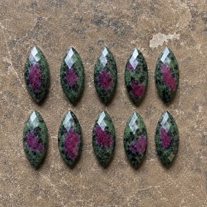 May include: Ten marquise-cut ruby zoisite gemstones arranged in two rows of five. Each stone features a faceted surface with a distinct color combination of deep forest green, black speckles, and vibrant magenta-pink inclusions throughout.